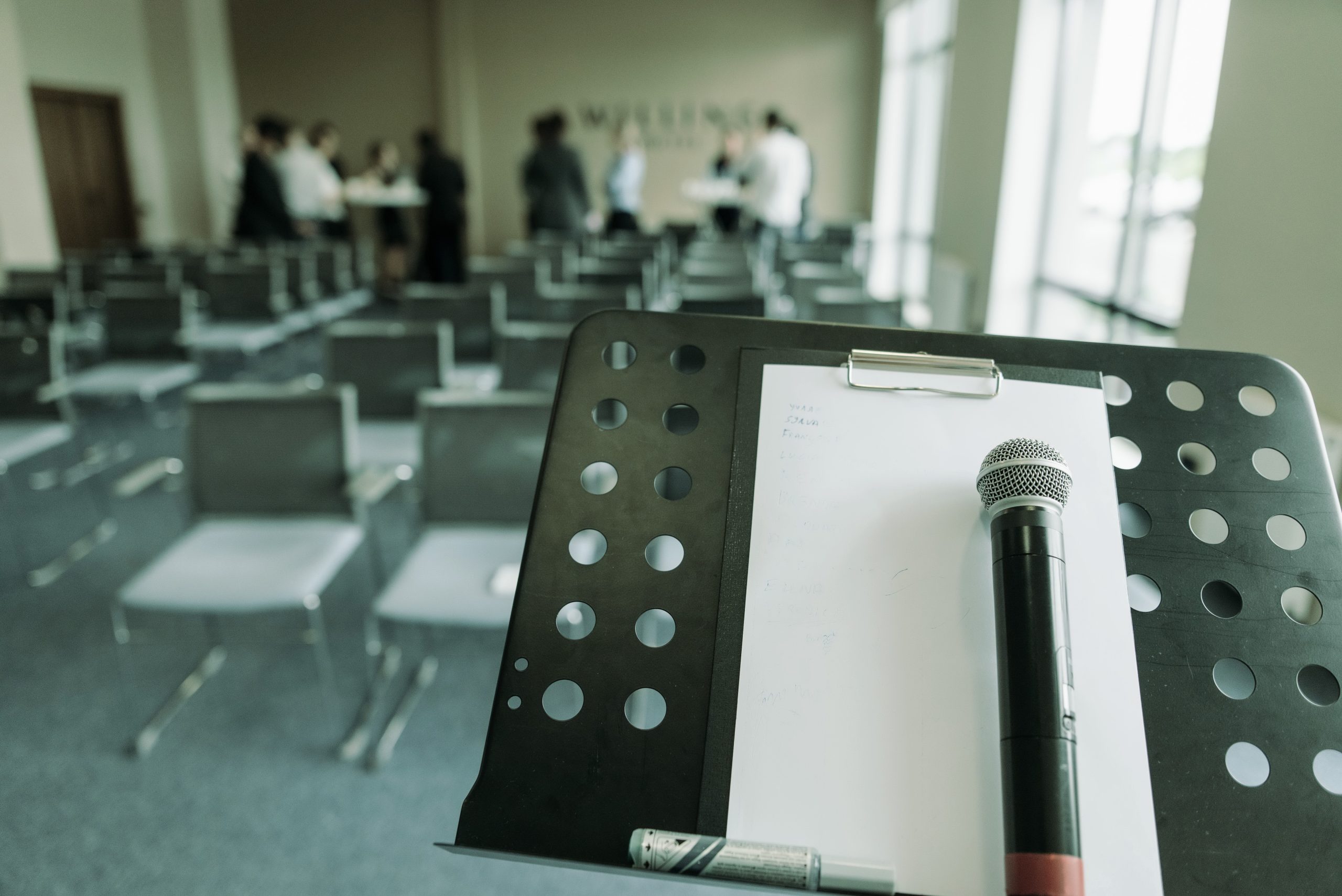 Microphone waiting on a stand before a talk, room filling in the background